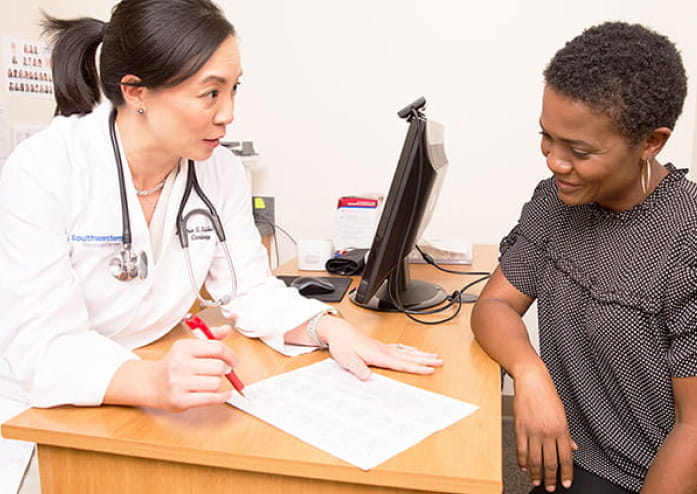 female doctor talking to young woman about health information on a paper at her desk