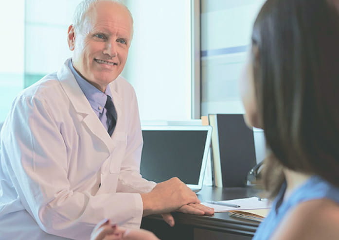 older male doctor sitting at his desk, smiling at patient